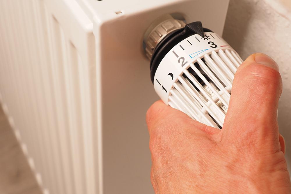 Hand regelt das Thermostat einer Heizung