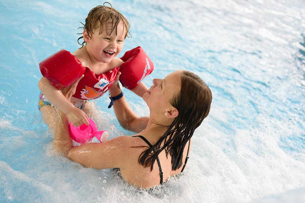Mutter und Kind mit Schwimmflügeln spielen im Kinderbecken
