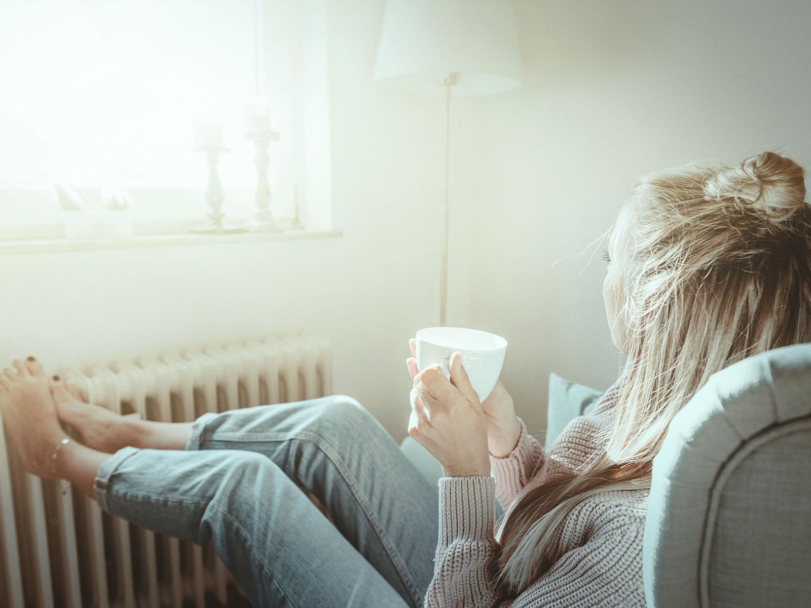 Frau macht es sich an wärmender Heizung mit Kaffee gemütlich