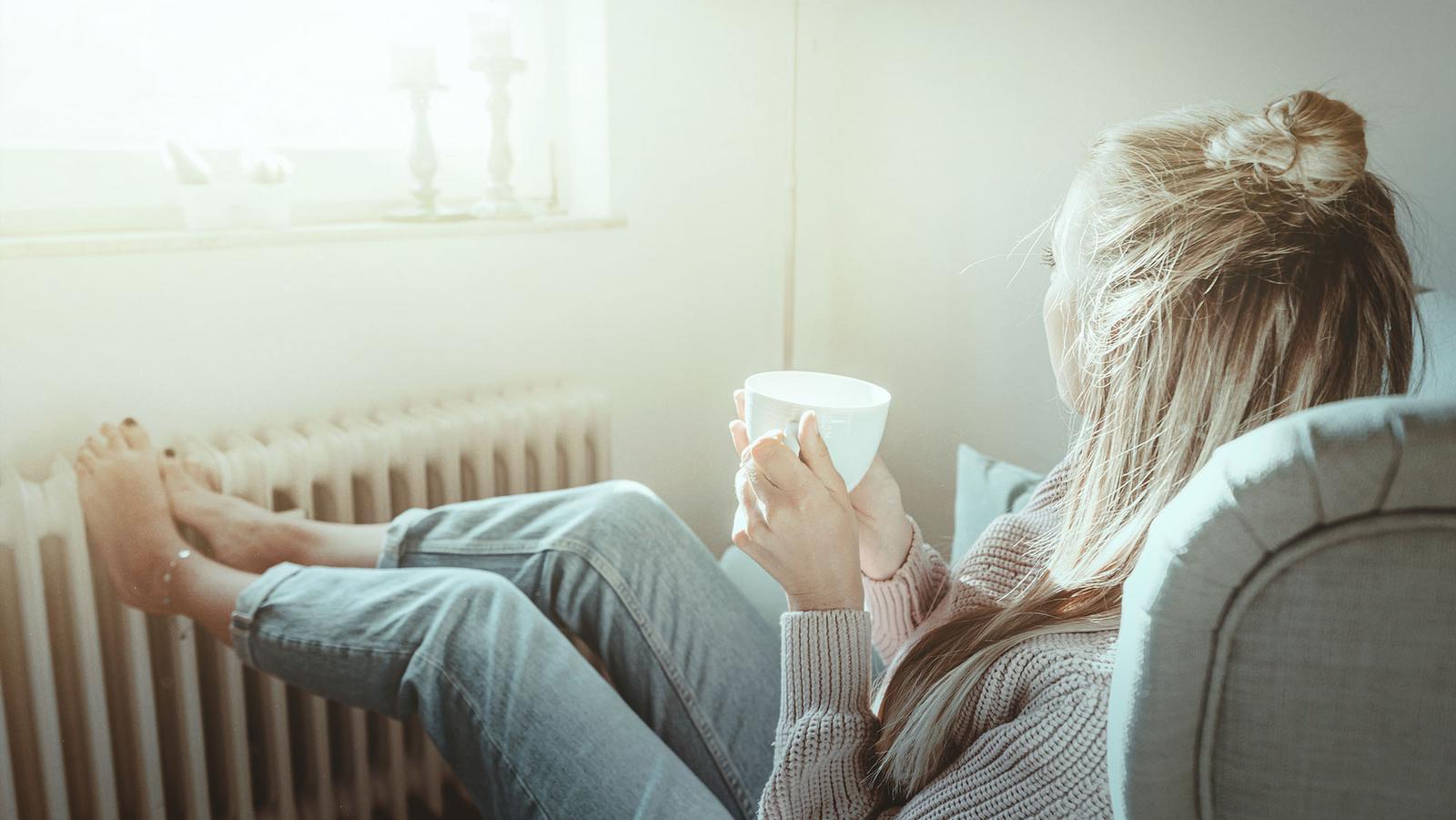 Frau macht es sich an wärmender Heizung mit Kaffee gemütlich