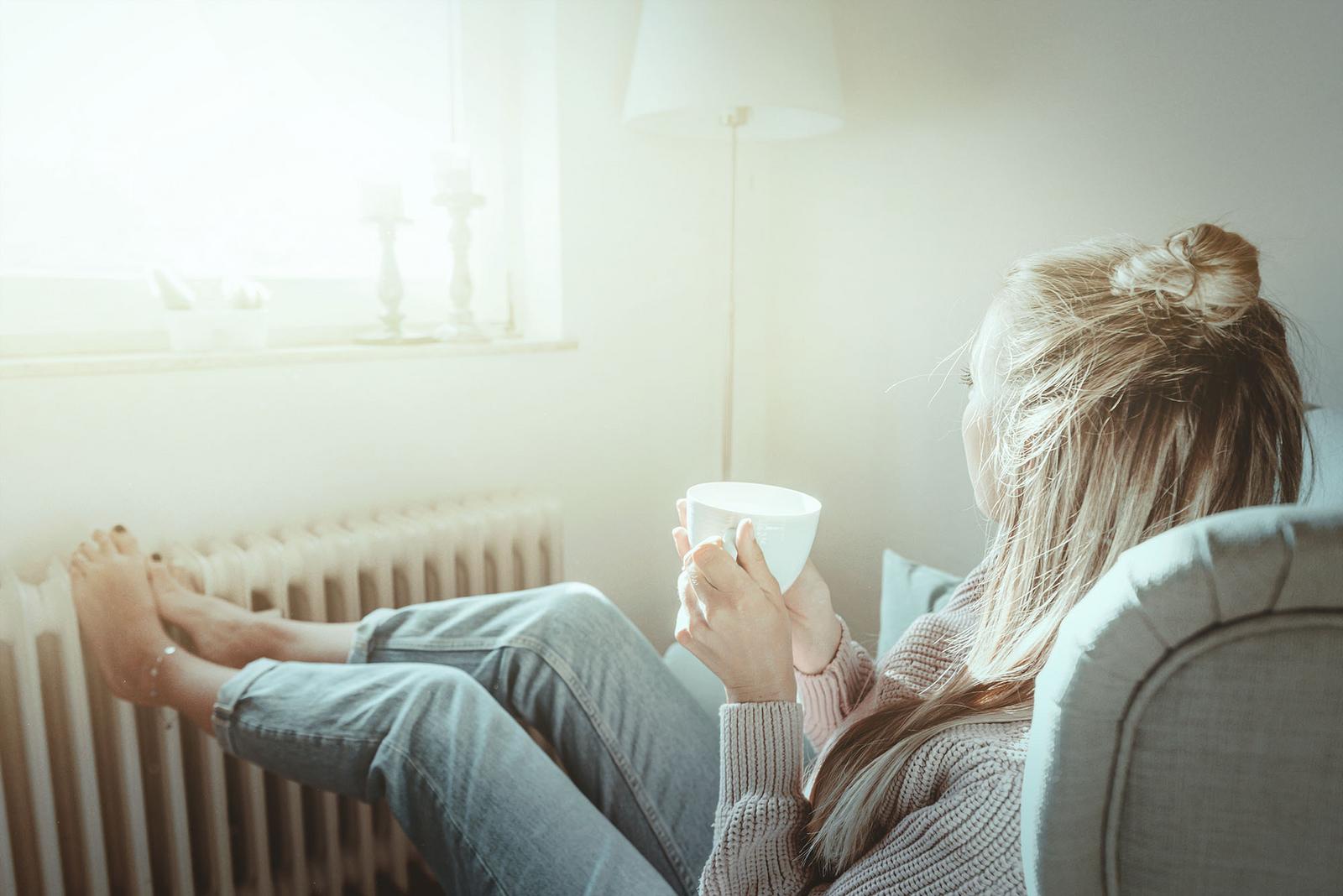 Frau macht es sich an wärmender Heizung mit Kaffee gemütlich