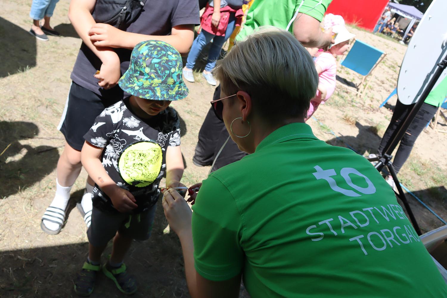 Mitarbeiterin mit grünem Stadtwerke Torgau T-Shirt gibt kleinem Kind einen Luftballon während der Stadtwerke Torgau Kinderparty