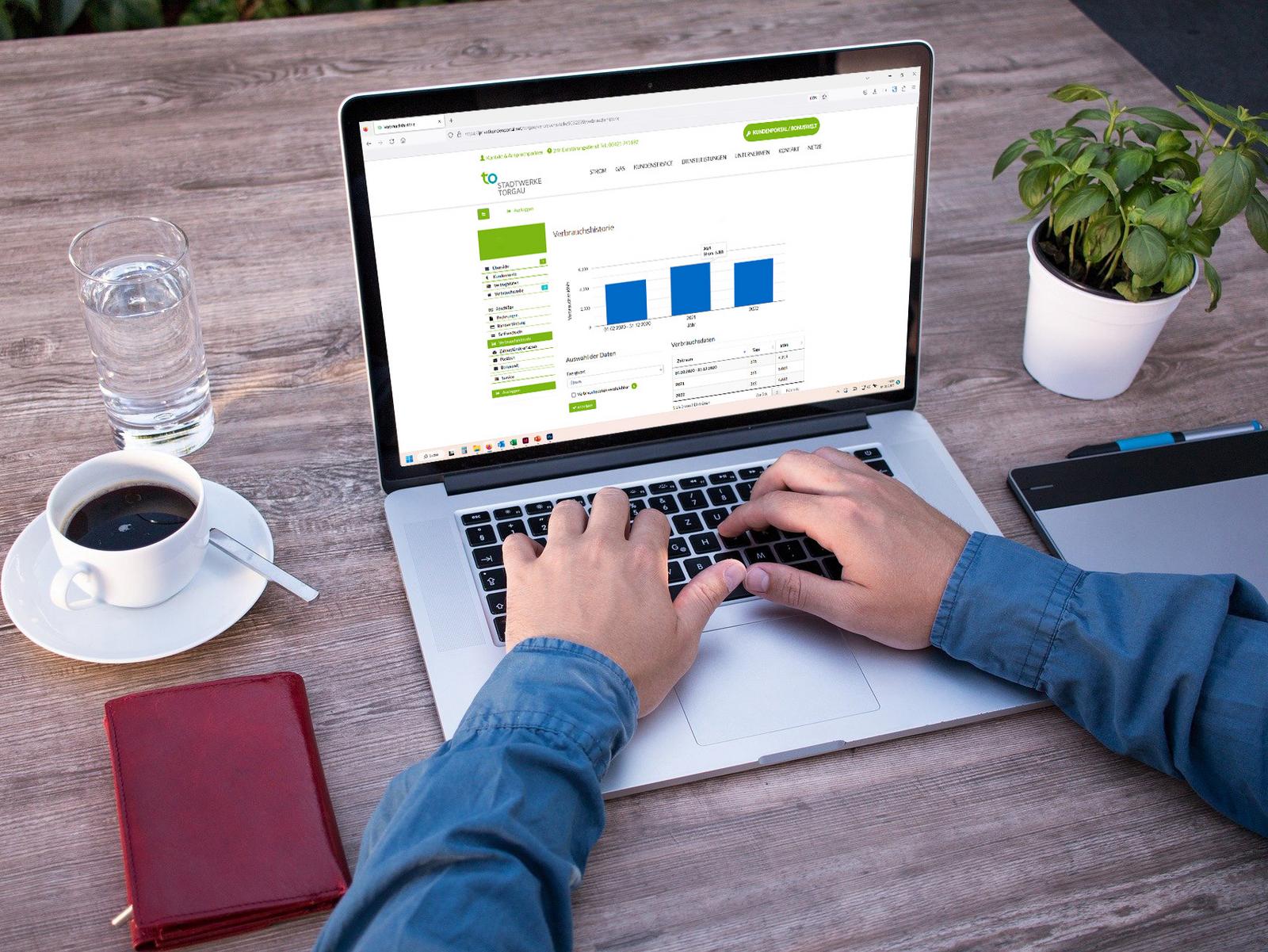 Notebook mit Login-Bereich des Kundenportals auf Schreibtisch mit Kaffee und Smartphone
